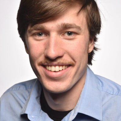 Photo of Owen Sahnow, a white man with red/brown hair and a mustache, wearing a light blue collared shirt.