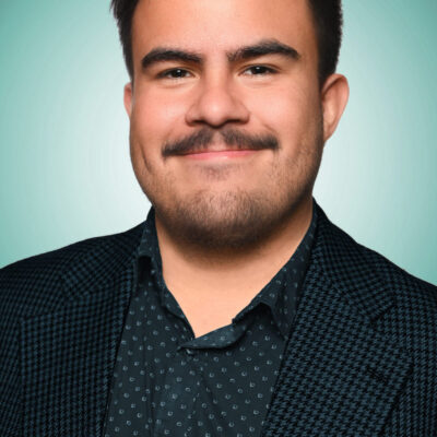 Photo of Paul Molina, a man with dark brown short hair and mustache, wearing a dark shirt and jacket.