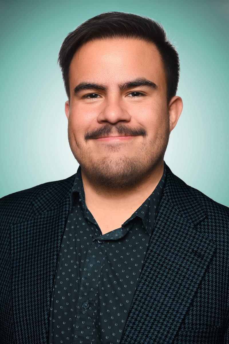 Photo of Paul Molina, a man with dark brown short hair and mustache, wearing a dark shirt and jacket.