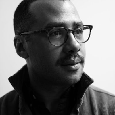 Black and white photo of Peter Andersen, a man with short dark hair and glasses, wearing a corduroy jacket with a popped collar.