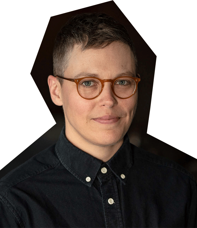 Photo of Nica Ross, a person with short brown hair and glasses, wearing a black collared, button down shirt