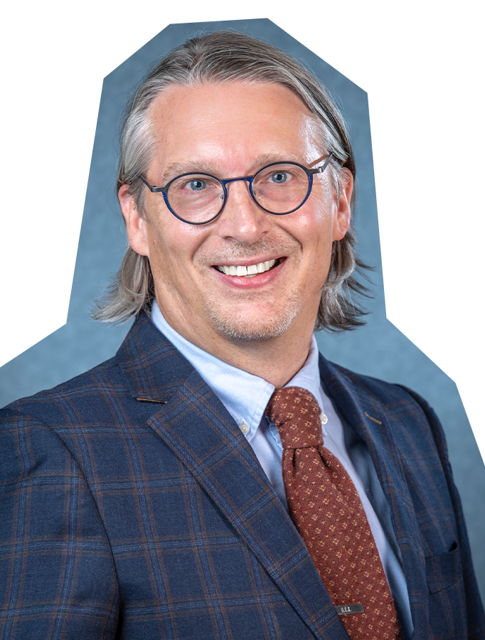 Photo of Brian Russman, a white man with medium length grey hair and glasses, wearing a navy blue patterned suit jacket and red tie.