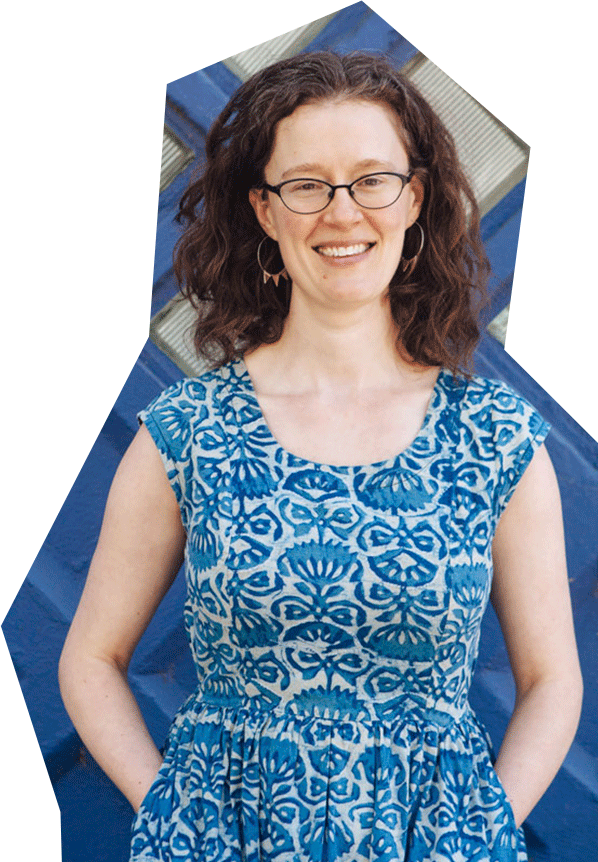 Photo of Emily Sapa, a white woman with red/brown hair and glasses, wearing a blue patterned dress and smiling.