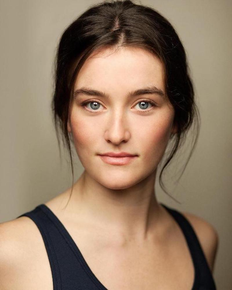 Photo of Sarah Pidgeon, a white woman with brown hair, pulled back, wearing a black tank top.