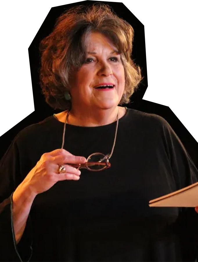 Photo of Ingrid Sonnichsen, a woman with brown hair, wearing a black blouse and holding a pair of glasses in her hand.