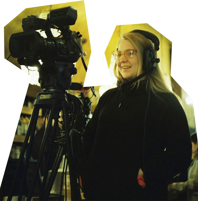 A photo of Aimee Thomas, a white woman with blond hair and glasses, wearing a headset and operating a camera.