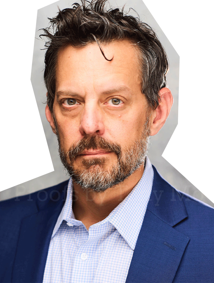 Photo of Sam Turich, a white man with brown hair and short beard, wearing a collared shirt and blue suit jacket.