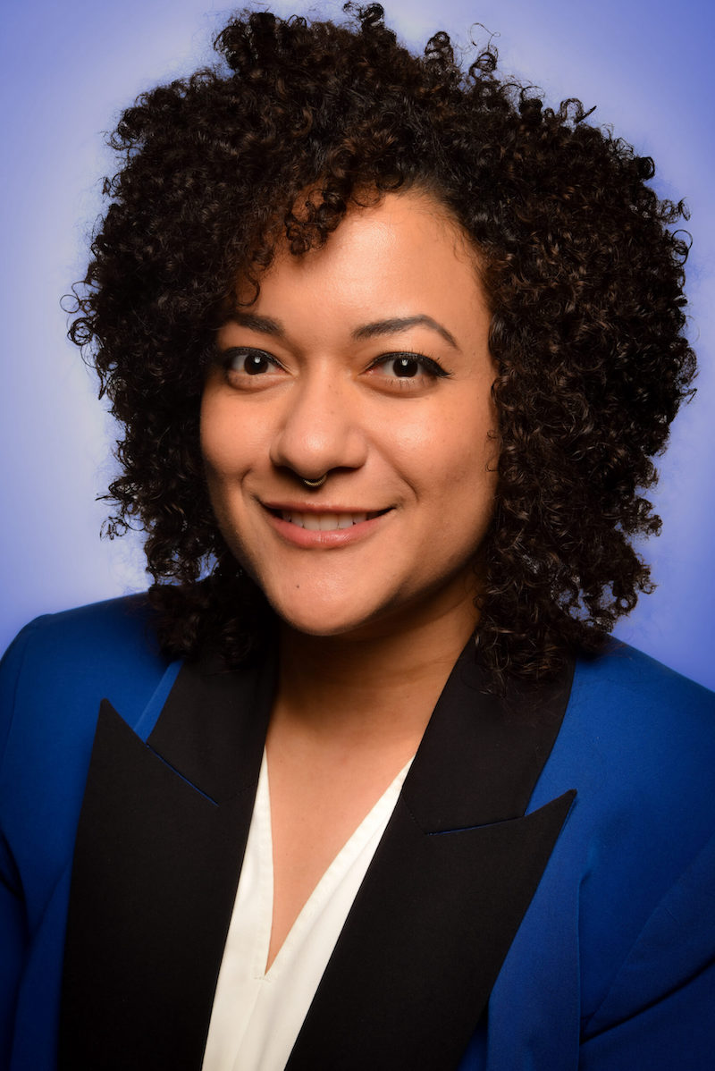 Photo of Xotchil Musser, a woman with short black curly hair wearing a blue blazer with a black lapel.