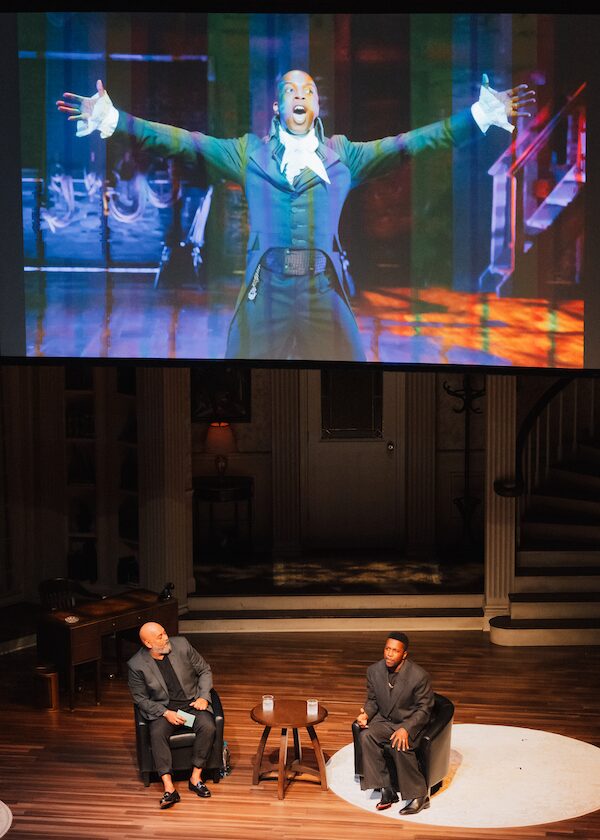 Robert Ramirez and Leslie Odom, Jr. seated on stage; a large projected image of Leslie as Aaron Burr in "Hamilton" is shown above them.