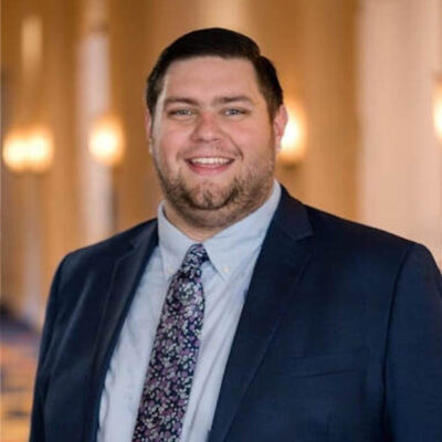 Photo of Ryan Dumas, a man with brown hair wearing a suit and tie.