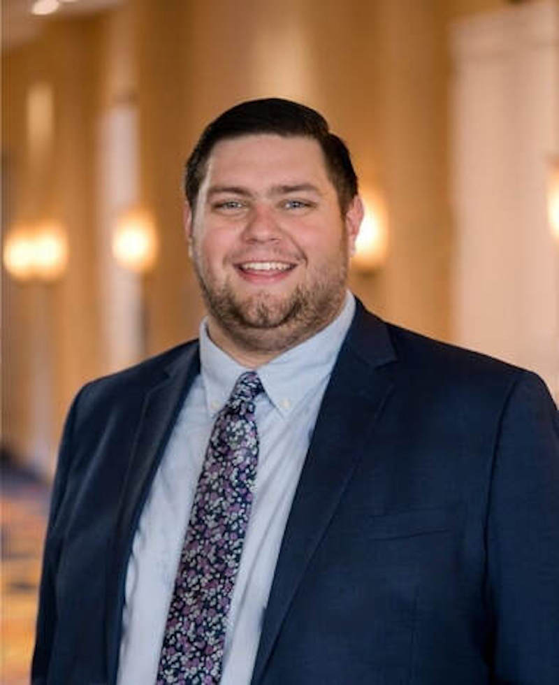 Photo of Ryan Dumas, a man with brown hair wearing a suit and tie.