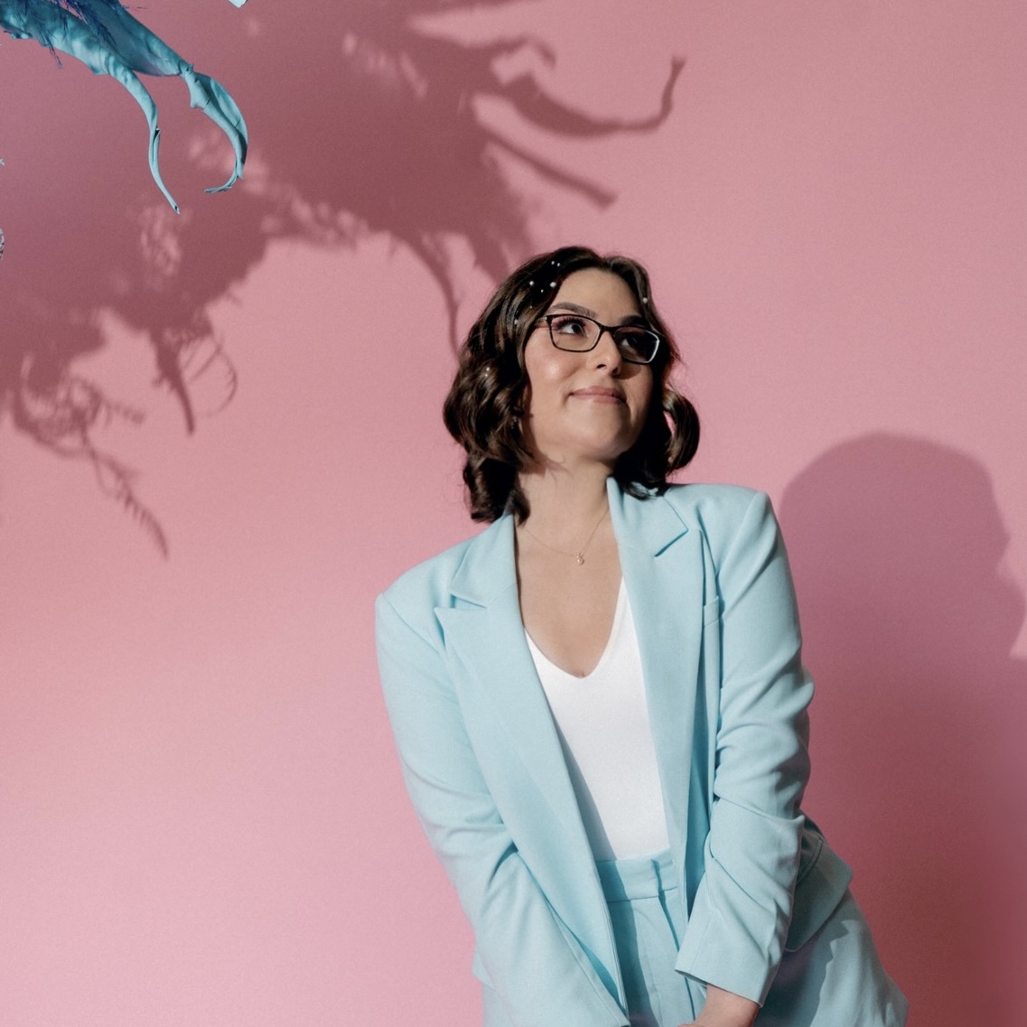 Photo of Samantha Williams, a woman with medium length brown hair wearing a baby blue suit, standing in front of a pink wall.