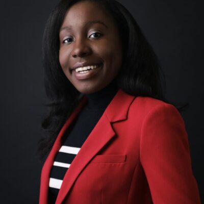 Photo of Kendra Chanae Chapman, a Black woman wearing a red blazer and a black and white striped top.