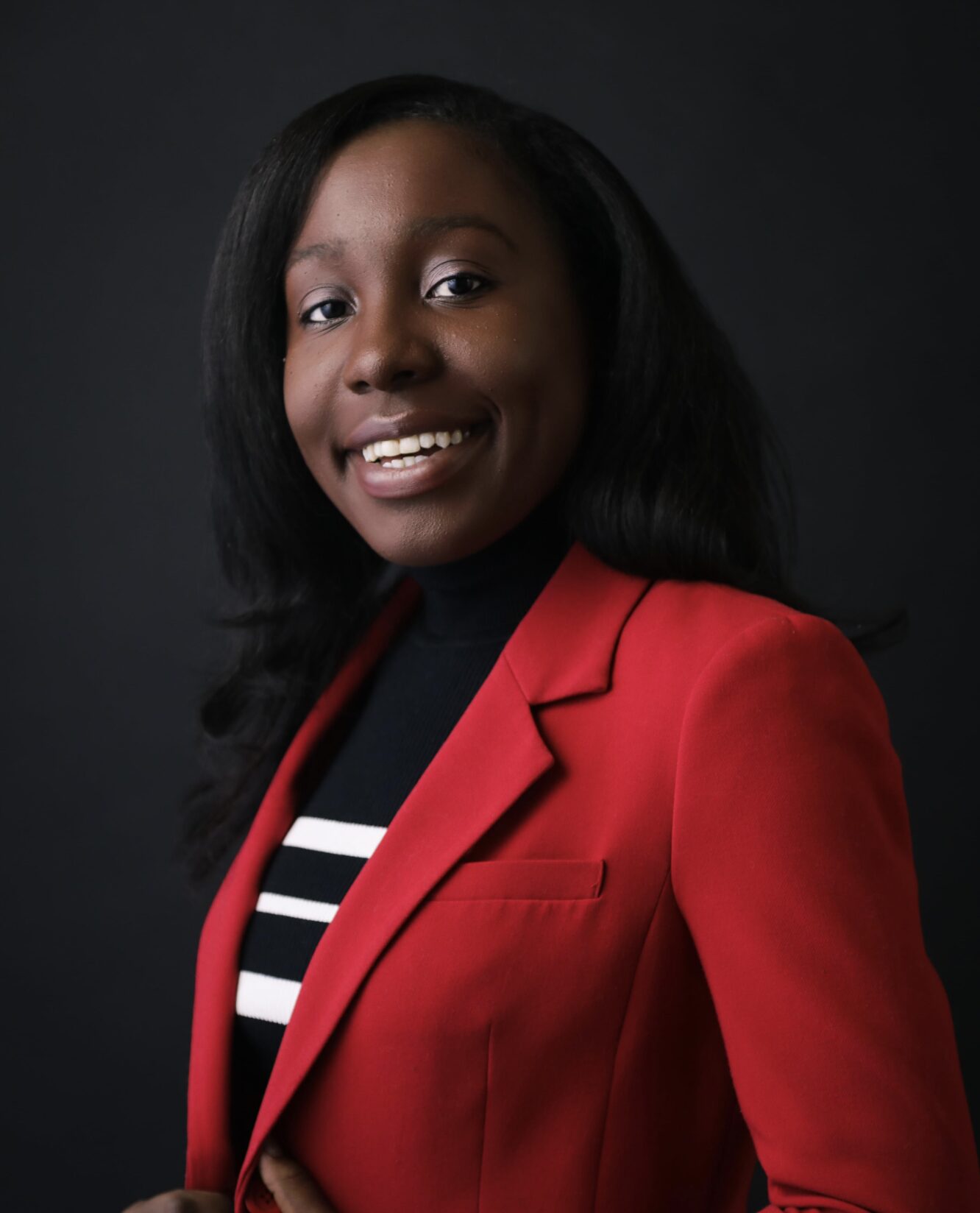 Photo of Kendra Chanae Chapman, a Black woman wearing a red blazer and a black and white striped top.