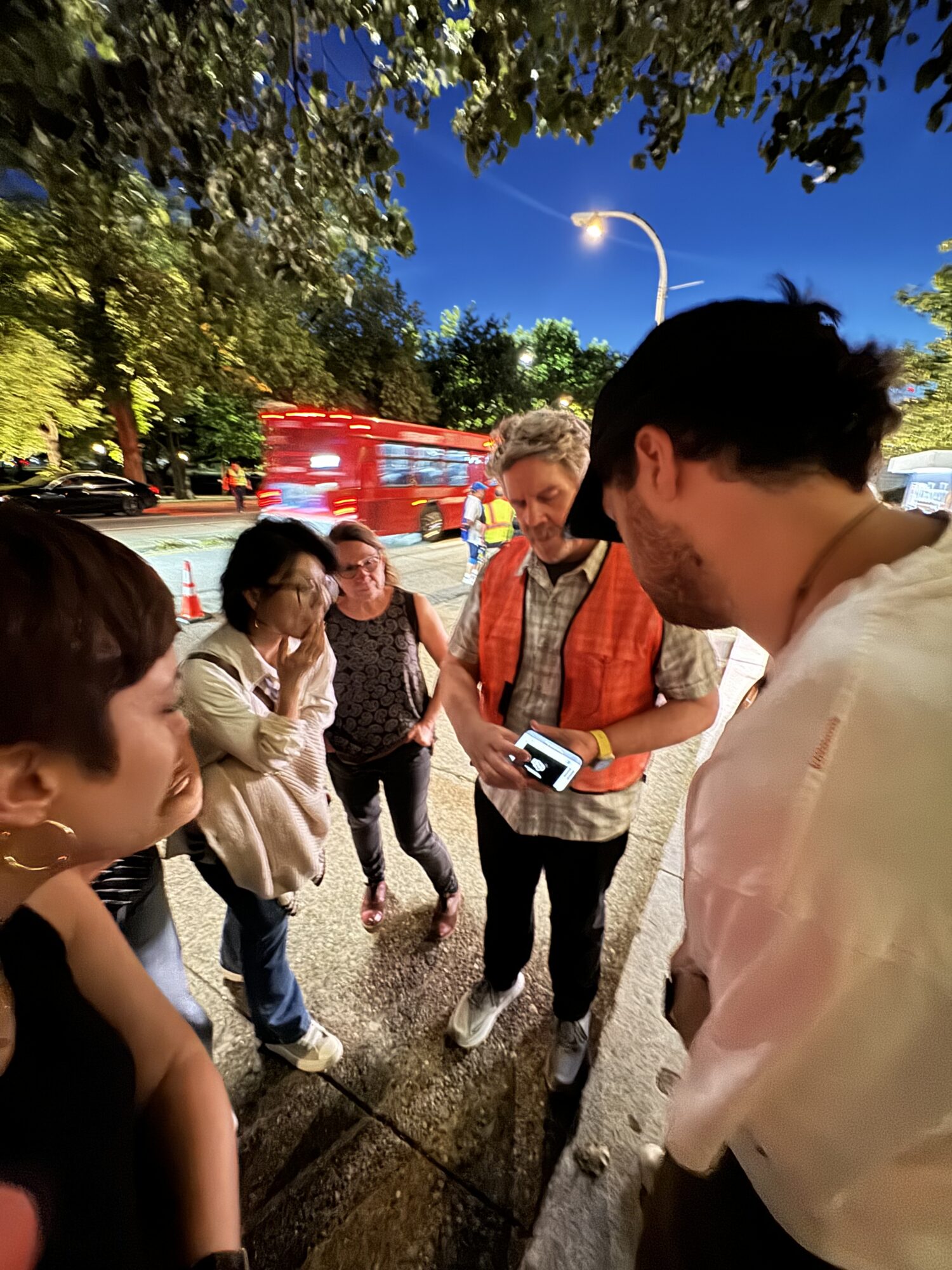 A group of students looks at John Wells's cell phone on a location shoot of "The Pitt."