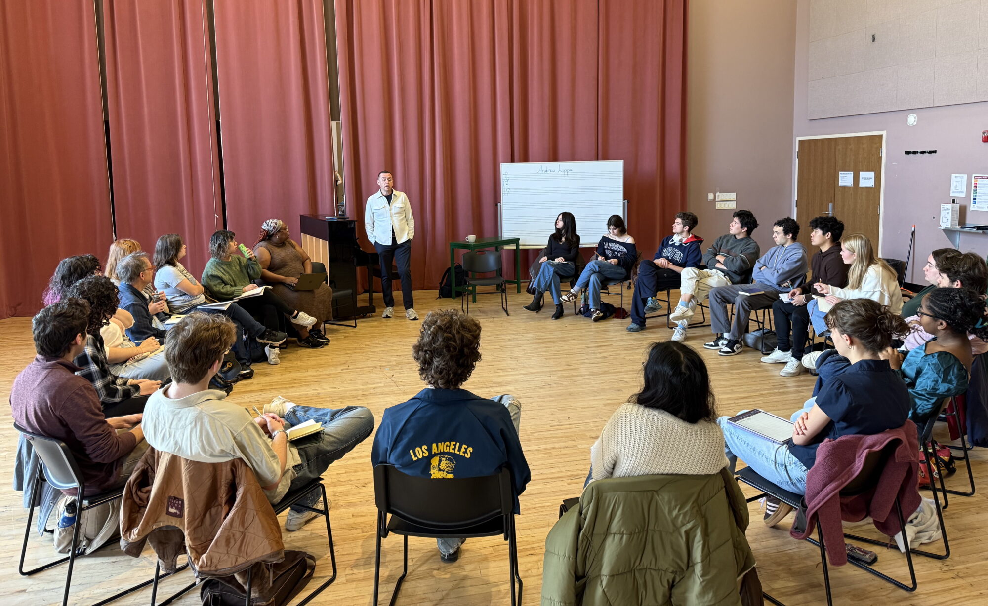 Students sit in a circle in a classroom, listening to Andrew Lippa