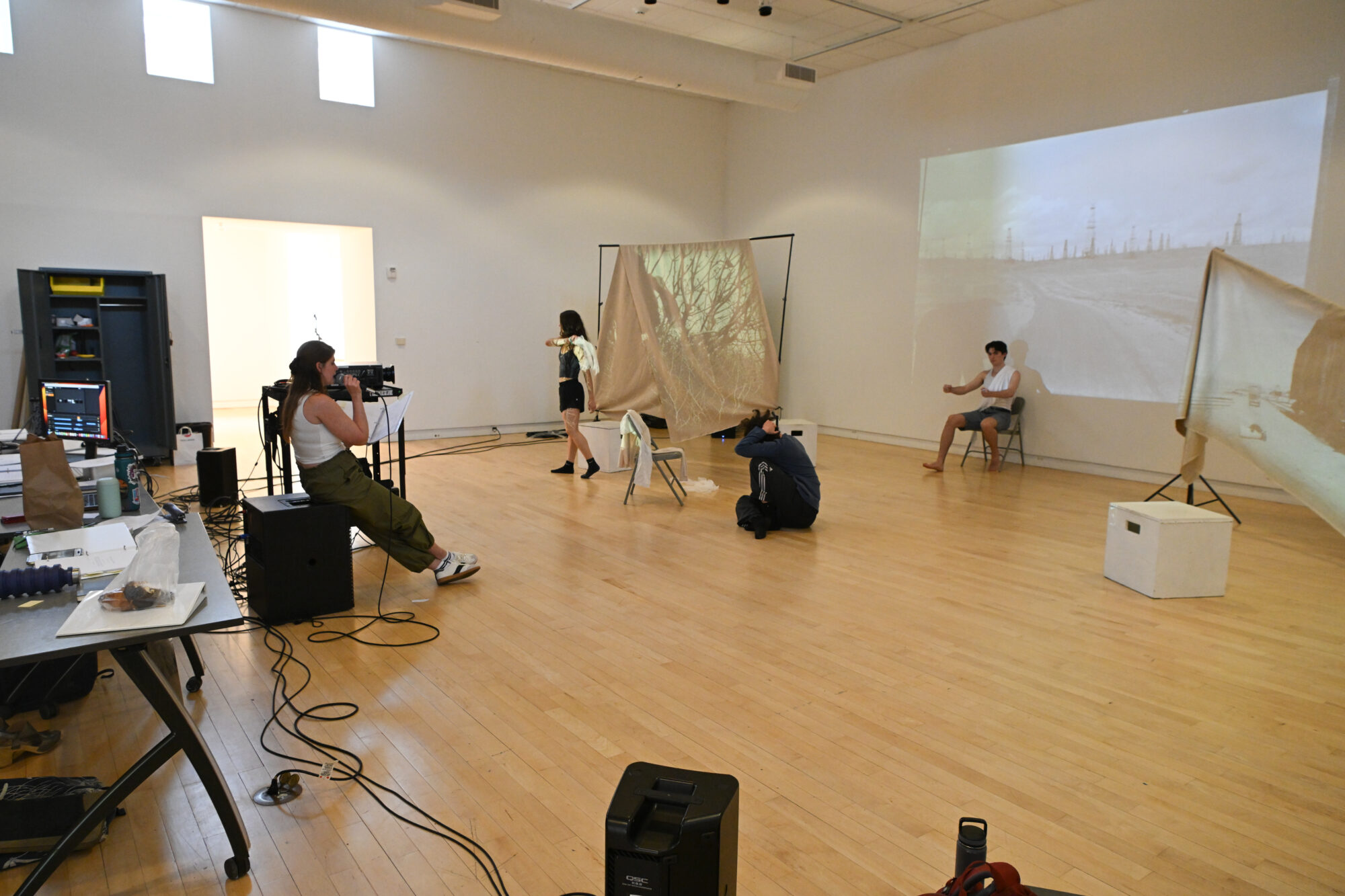 Actors, designers, and a director work in an art gallery space with projections.